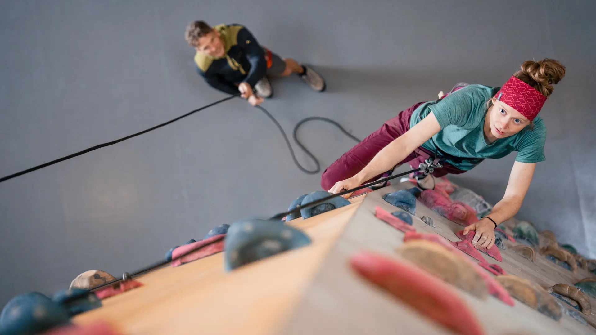 Eine Frau klettert in einer Kletterhalle, ihr Partner sichert sie. | © DAV / Julian Rohn